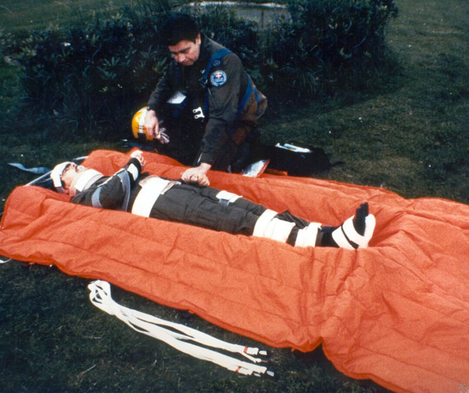 CAS-Straps in the field: a paramedic securing a casualty onto an orange vacuum stretcher